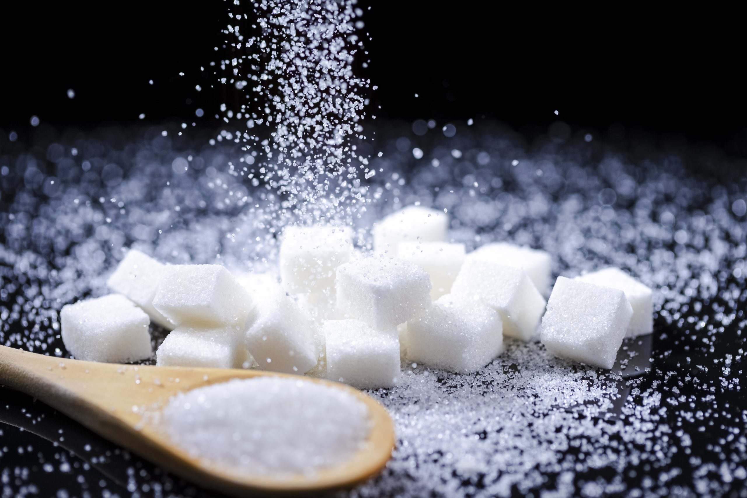 Macro Shot of White Cube Sugar And Falling Sand Sugar Along With Filled Wooden Measure Spoon. Against Black Background. Macro Shot of White Cube Sugar And Falling Sand Sugar Along With Filled Wooden Measure Spoon. Against Black Background. Horizontal Orientation
